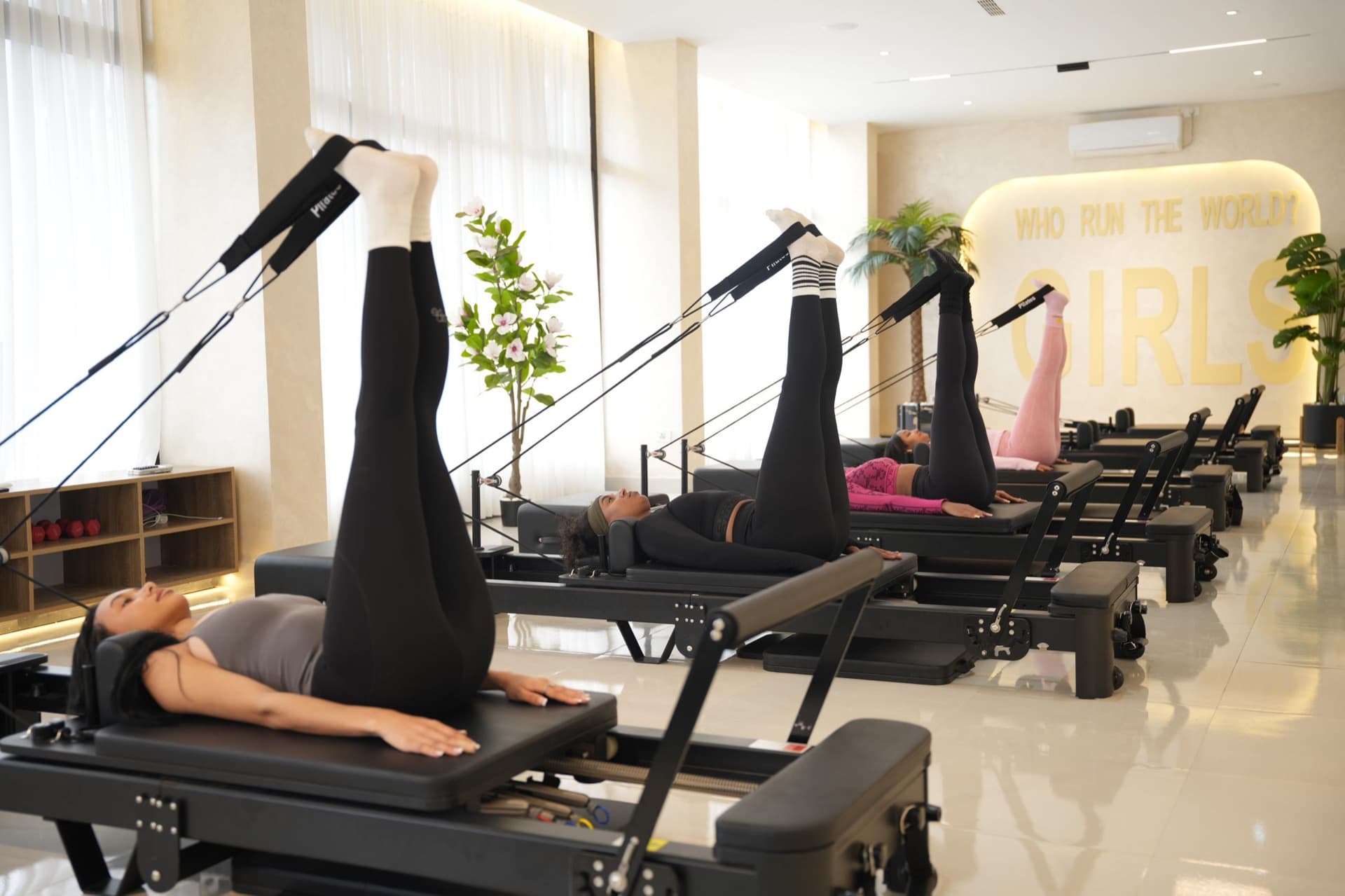 A reformer class in session at Ethio Pilates Studio, legs lifted in unison beneath the brass 'Who run the world' wall