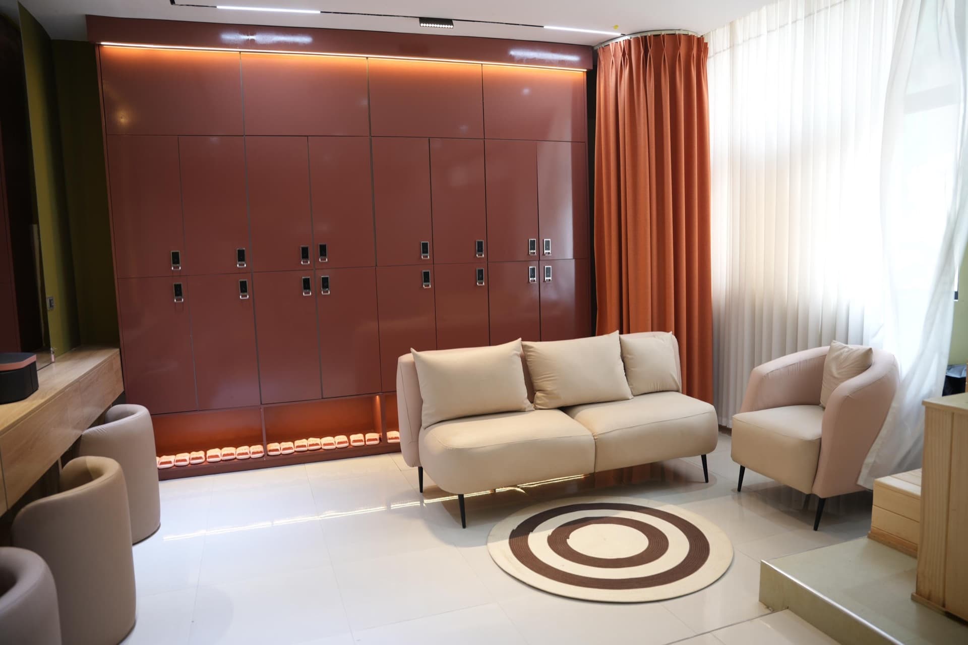 The locker lounge — glossy oxblood lockers, soft seating, and quiet light